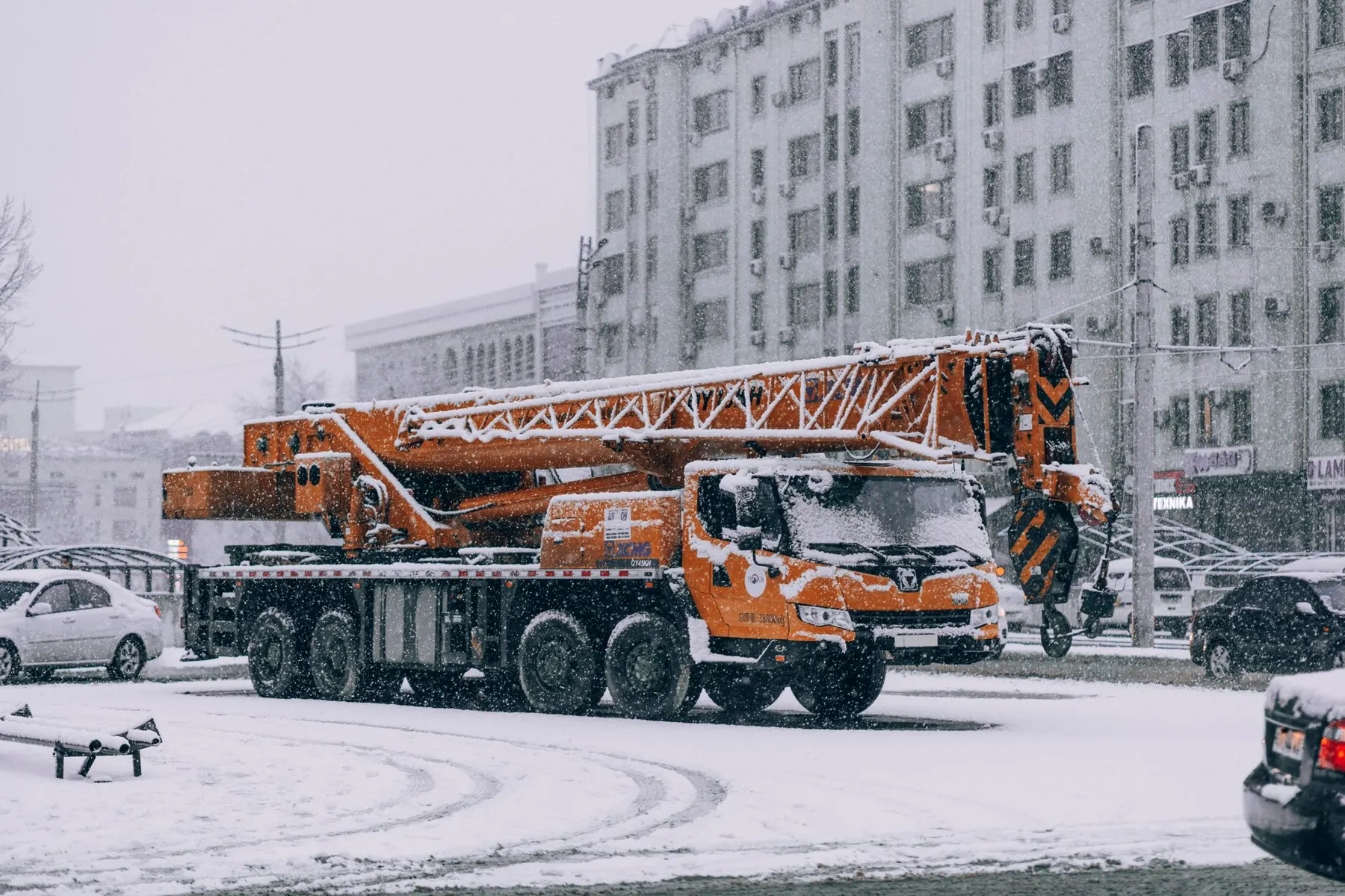 Urban scene in Samarkand during heavy snowfall with construction truck prominent against snowy backdrop.