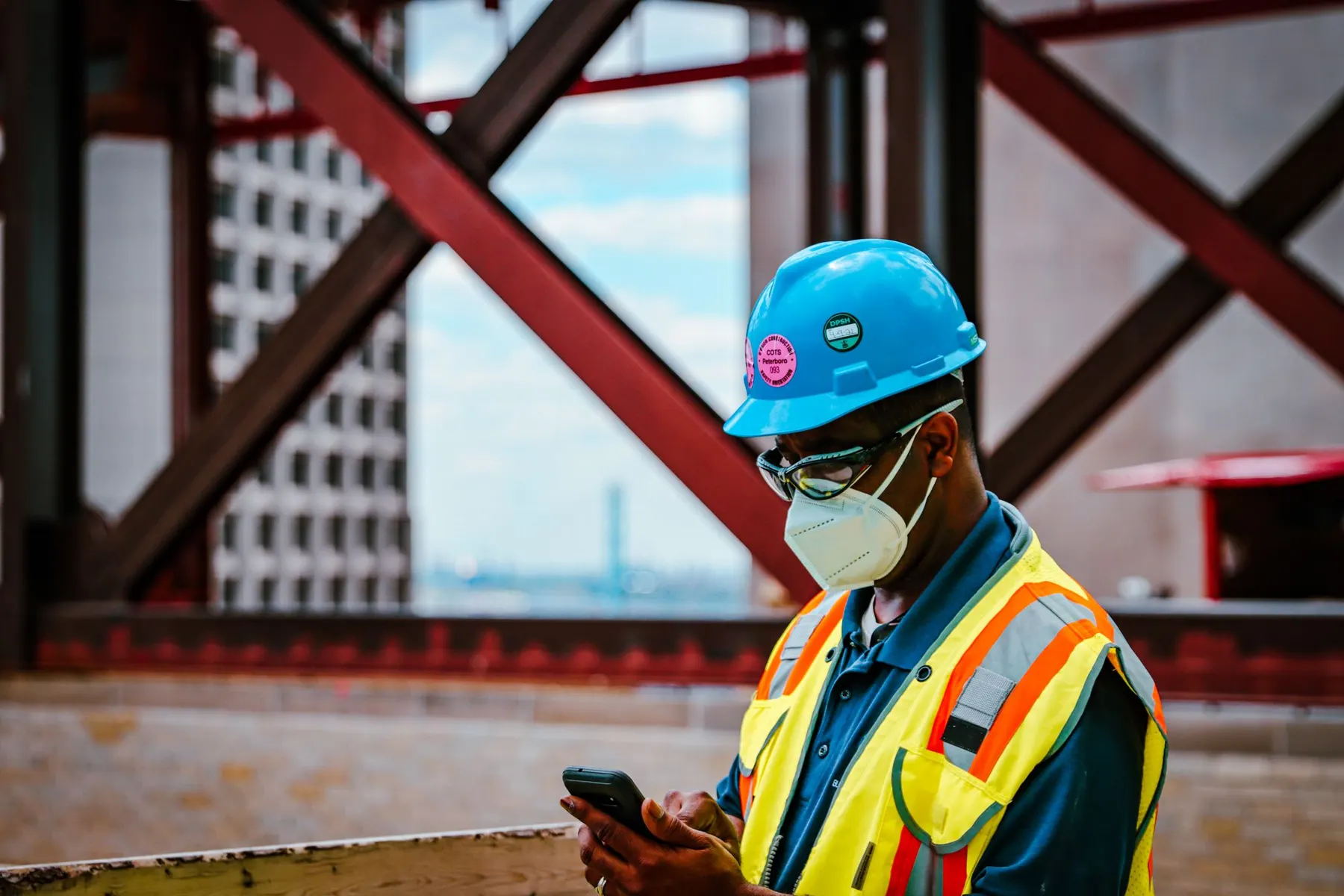 Construction worker in safety gear checking smartphone on a Detroit site.